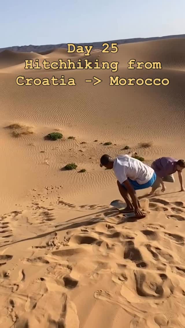 Two figures crouched on boards on a dune face, footprints running down the sand behind them.